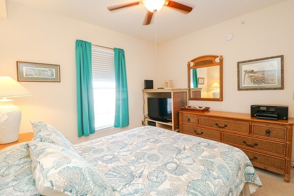 A bedroom with a bed, a dresser, a television, and a ceiling fan. - Seaside at Anastasia A301 (St Augustine)