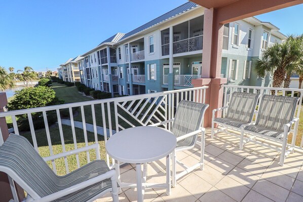A balcony with white chairs and a table, overlooking a row of blue and white buildings with balconies. - Seaside at Anastasia D205 New Master Bathroom! (St Augustine)