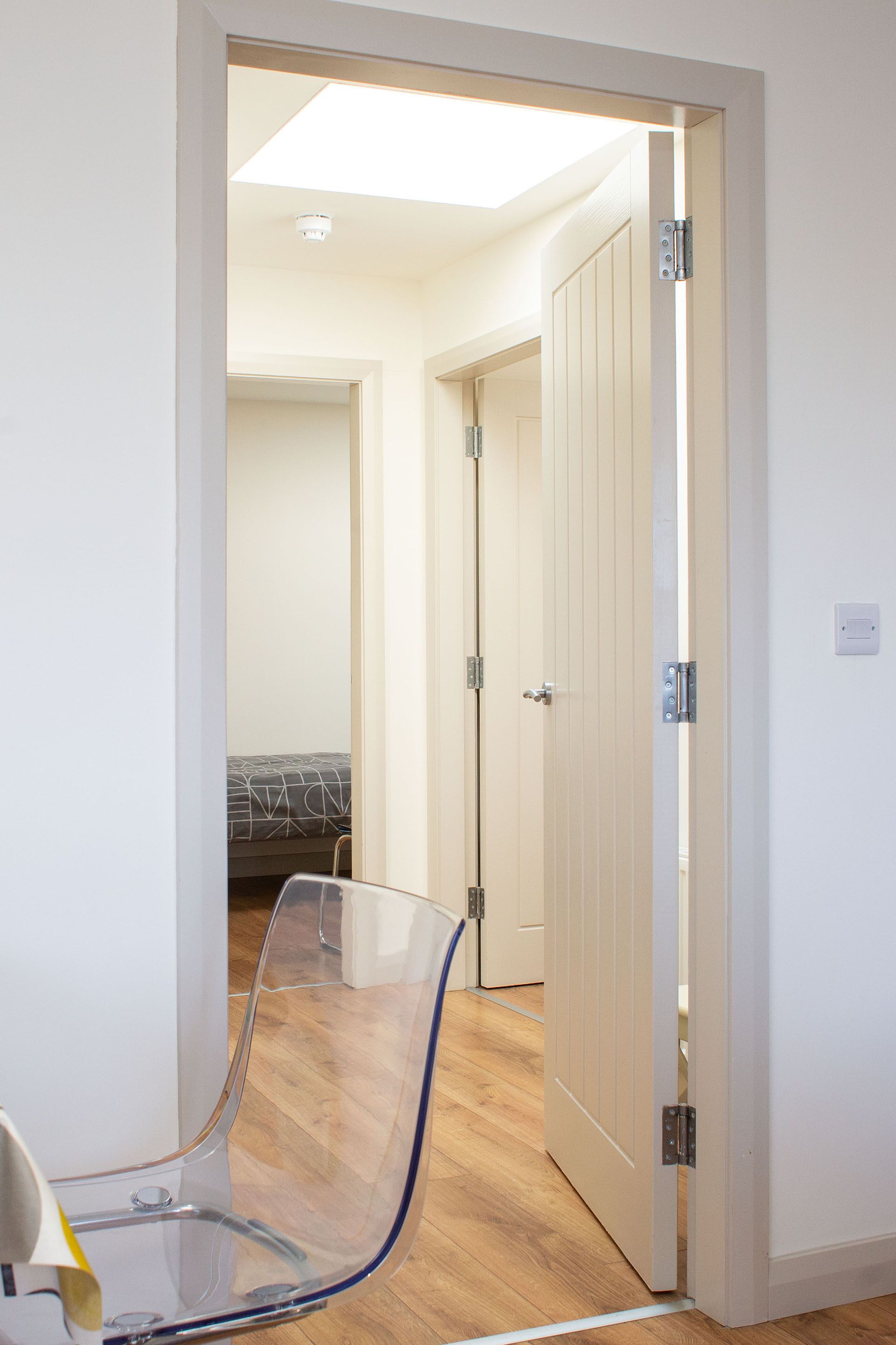A room with a clear glass chair, wooden flooring, and a door leading to another room.