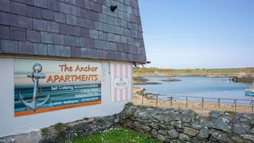 En fastighet vid havet som heter ”The Anchor Apartments”, med en skylt som annonserar ut hyreslägenheter med självhushåll, havsutsikt och en stenmur i förgrunden.