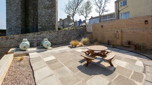 A courtyard with a stone wall, a wooden table and benches, and two large gas cylinders. - The Anchor Apartments (Downpatrick)