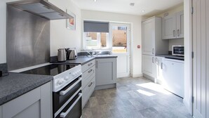 A modern kitchen with a stainless steel range hood, a built-in oven, a microwave, and a window providing natural light. - The Anchor Apartments (Downpatrick)