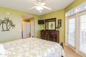 A bedroom with a bed, a dresser, a ceiling fan, a TV, and a door leading to another room. - Seaside at Anastasia E302- Renovated Luxury Penthouse Condo (St Augustine)