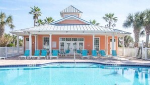 Uma área de piscina com um edifício de fachada vermelha e teto branco, cercada por palmeiras.
