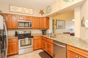 A kitchen with wooden cabinets, a stainless steel microwave, a stove, and a coffee maker. - Seaside at Anastasia E302- Renovated Luxury Penthouse Condo (St Augustine)