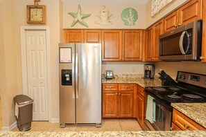 Una cocina con un refrigerador de acero inoxidable, armarios de madera, un microondas, una estufa y un bote de basura.