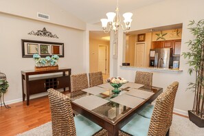 A dining area with a glass-top table, woven chairs, a chandelier, and a mirror above the table.