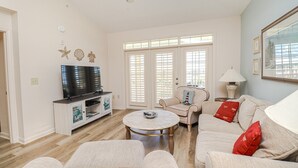 Een ruime woonkamer met een flatscreen televisie, een ronde salontafel en een beige bank met rode kussens.