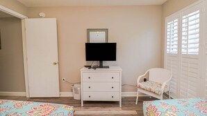 Ein Schlafzimmer mit einem weißen Schminktisch, einem Fernseher, einem Sessel mit Blumenkissen und einem Bett mit Blumendecke.