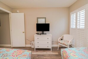 A bedroom with a white dresser, a television, a chair with a floral cushion, and a bed with a floral bedspread. - Just Steps From the Pool & Beach!! Also has Boat Ramp and Fishing Pier! Trade Winds 51 (St. Augustine)