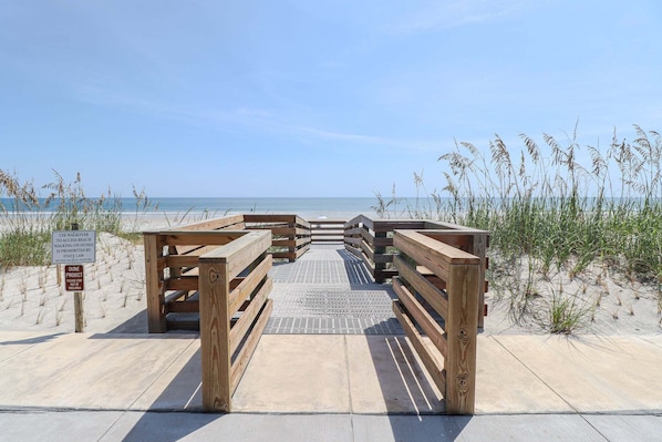 A wooden boardwalk leading to a beach with a sign indicating dune access is prohibited.