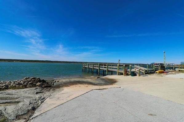 A concrete pier extending into calm water, a sandy beach, and a clear blue sky.
