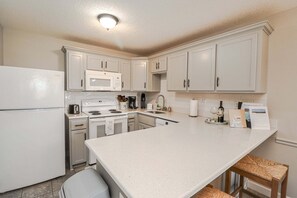 A compact kitchen with white cabinetry, a microwave, a stove, and a coffee maker.