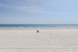 A wide sandy beach with a few people and a beach umbrella.