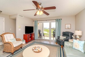 A living room with a ceiling fan, a television, wicker furniture, a red cabinet, and a view through a glass door. - Just Steps From the Pool & Beach!! Also has Boat Ramp and Fishing Pier! Trade Winds 51 (St. Augustine)