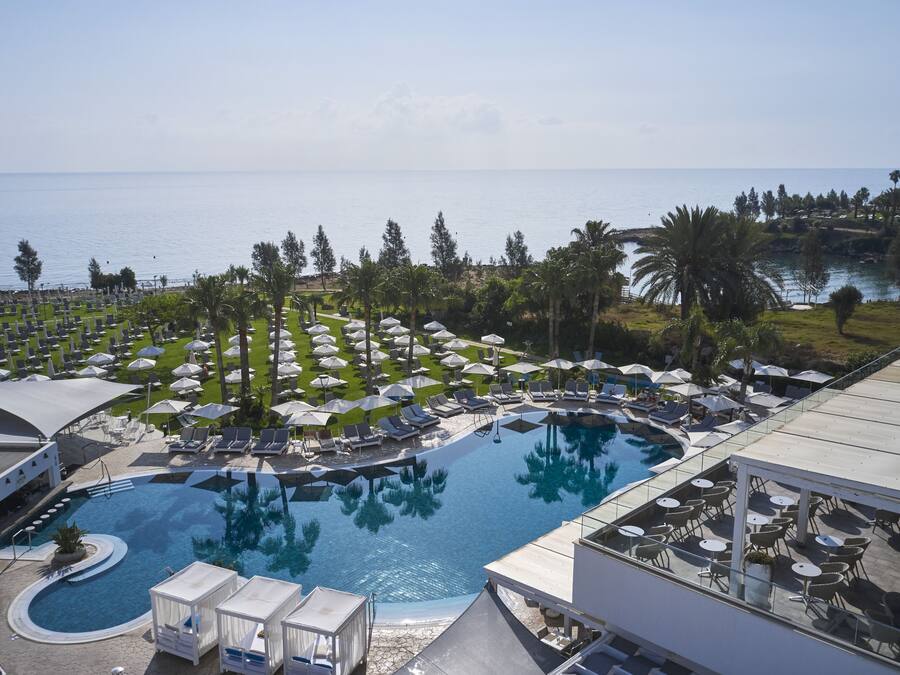 A resort pool area with lounge chairs and umbrellas, a clear view of the sea, and a landscaped garden.