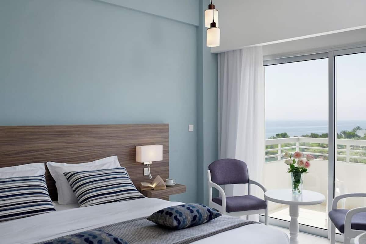 A hotel room with a large bed, a nightstand with a lamp, a chair, and a view of the ocean.