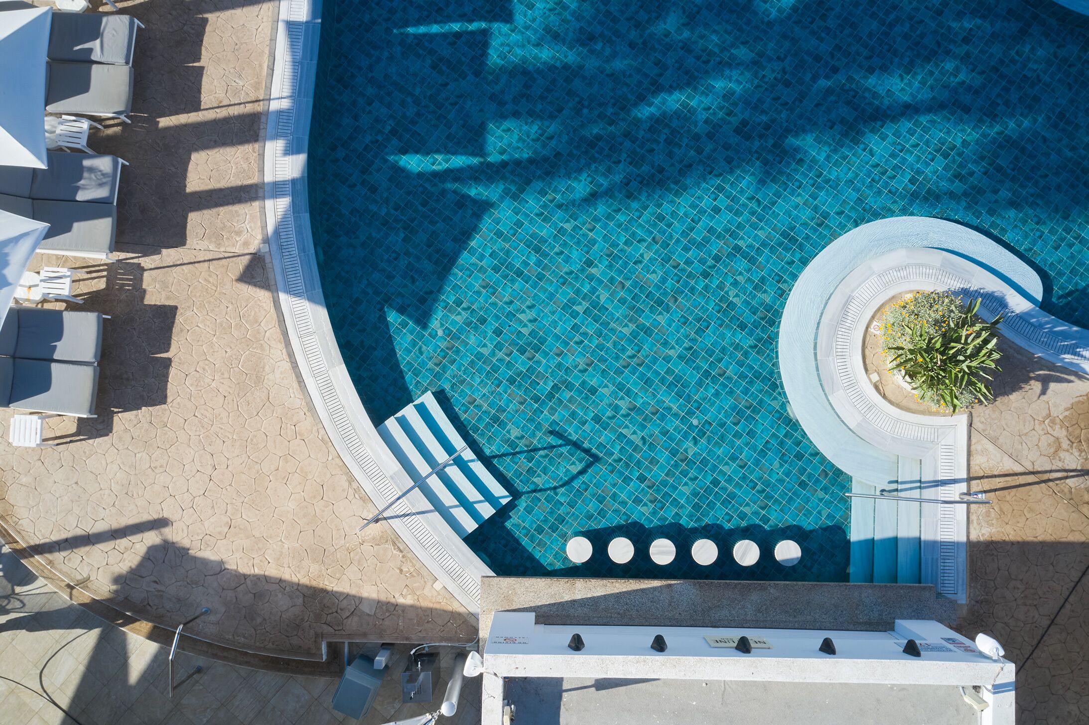 Vista aérea de una piscina con solárium empinado, sillas de descanso y una fuente circular.