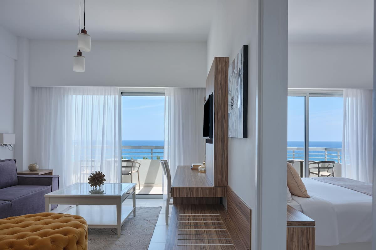 A modern hotel room with a balcony, a sofa, a coffee table, and a TV.