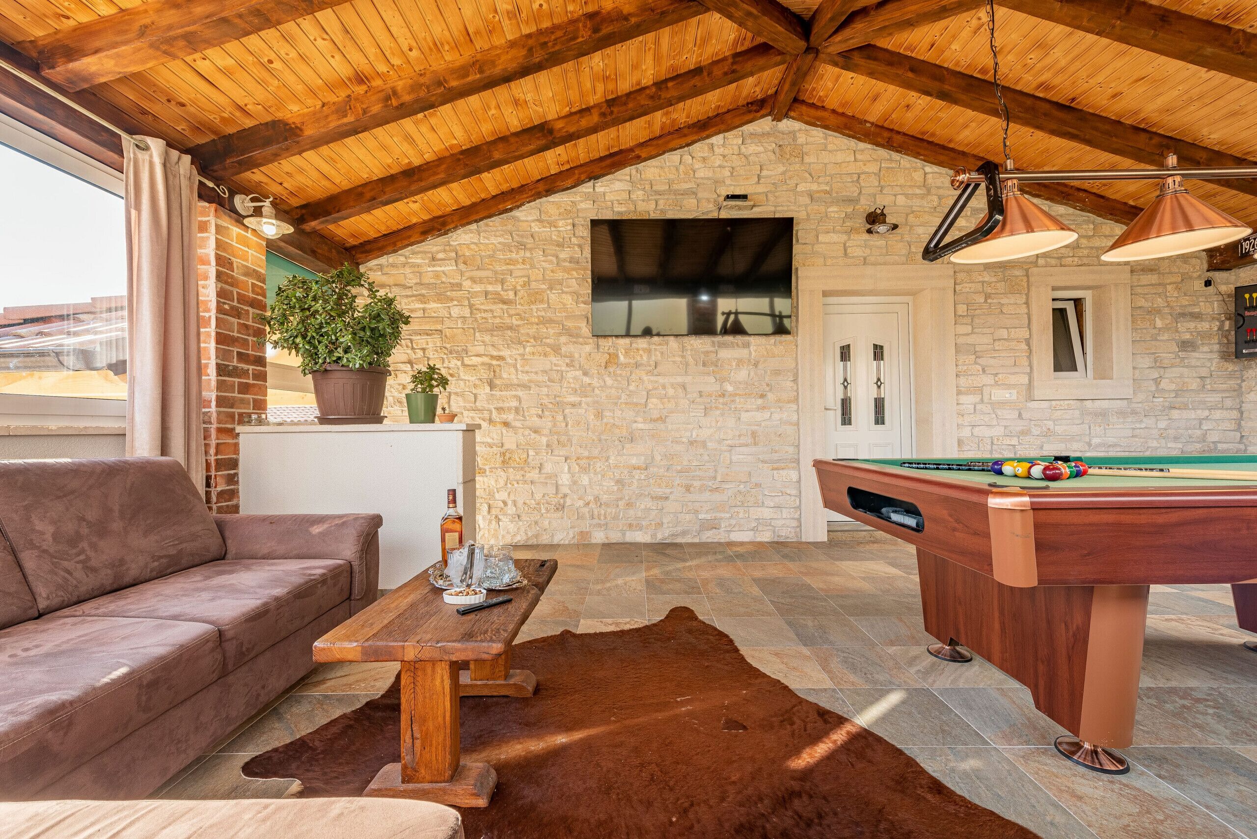 A cozy indoor space with a pool table, a sofa, and a wooden ceiling.
