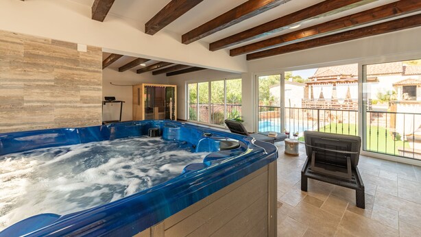 Ein Whirlpool in einem großzügigen Raum mit Holzbalken und großen Fenstern mit Blick auf einen Poolbereich.