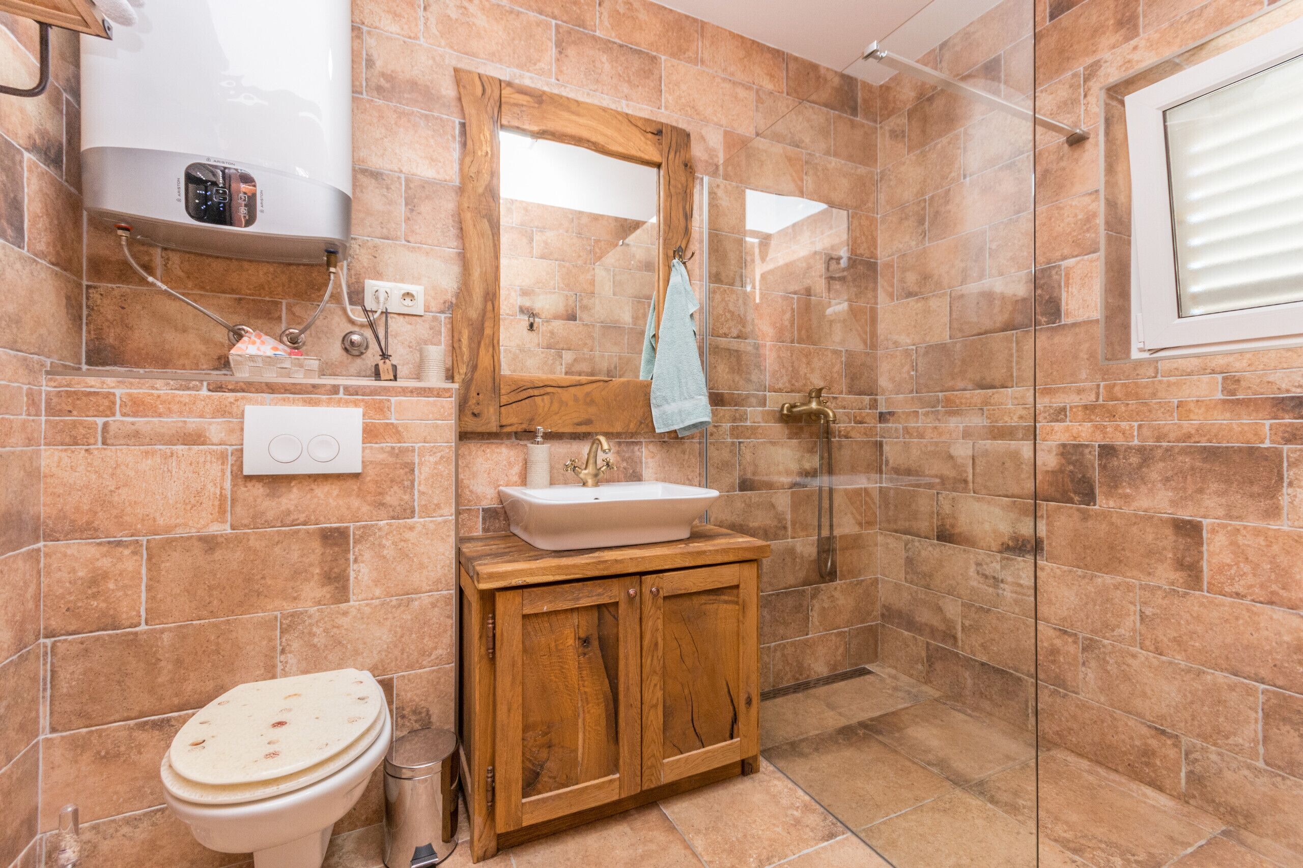 A bathroom with a wooden vanity, a white sink, a mirror, and a shower area.