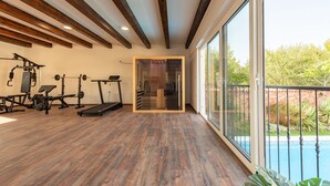 Ein Fitnessraum mit Holzboden, Trainingsgeräten und einem großen Fenster mit Blick auf einen Pool.