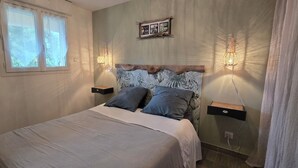 A bedroom with a bed, two bedside tables, a window, a wall-mounted shelf with pictures, and two wall-mounted lamps. - Nice and quiet 3-room apartment with swimming pool Casa Lisa  (Prunelli-di-Fiumorbo)