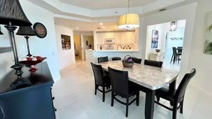 A dining area with a marble table and black chairs, a chandelier, and a kitchen in the background. - WELCOME to PARADISE! Beautiful sunrise AND sunset views   (Ft. Myers)