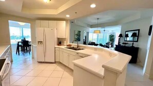 A modern kitchen with white cabinetry, a large island, and a dining area with a view. - WELCOME to PARADISE! Beautiful sunrise AND sunset views   (Ft. Myers)