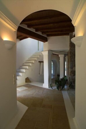 Stunning interior corridor with a high ceiling and wooden beam structure, featuring a simple staircase and stone column.