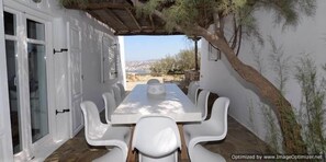 Enjoy meals in a serene setting with a long table and comfortable chairs, surrounded by a picturesque view.