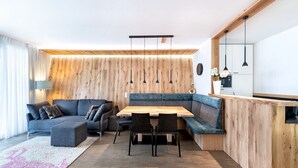 Una sala moderna con una pared de acento de madera, una mesa de comedor con sillas, un sofá y una zona de cocina con lámparas colgantes.