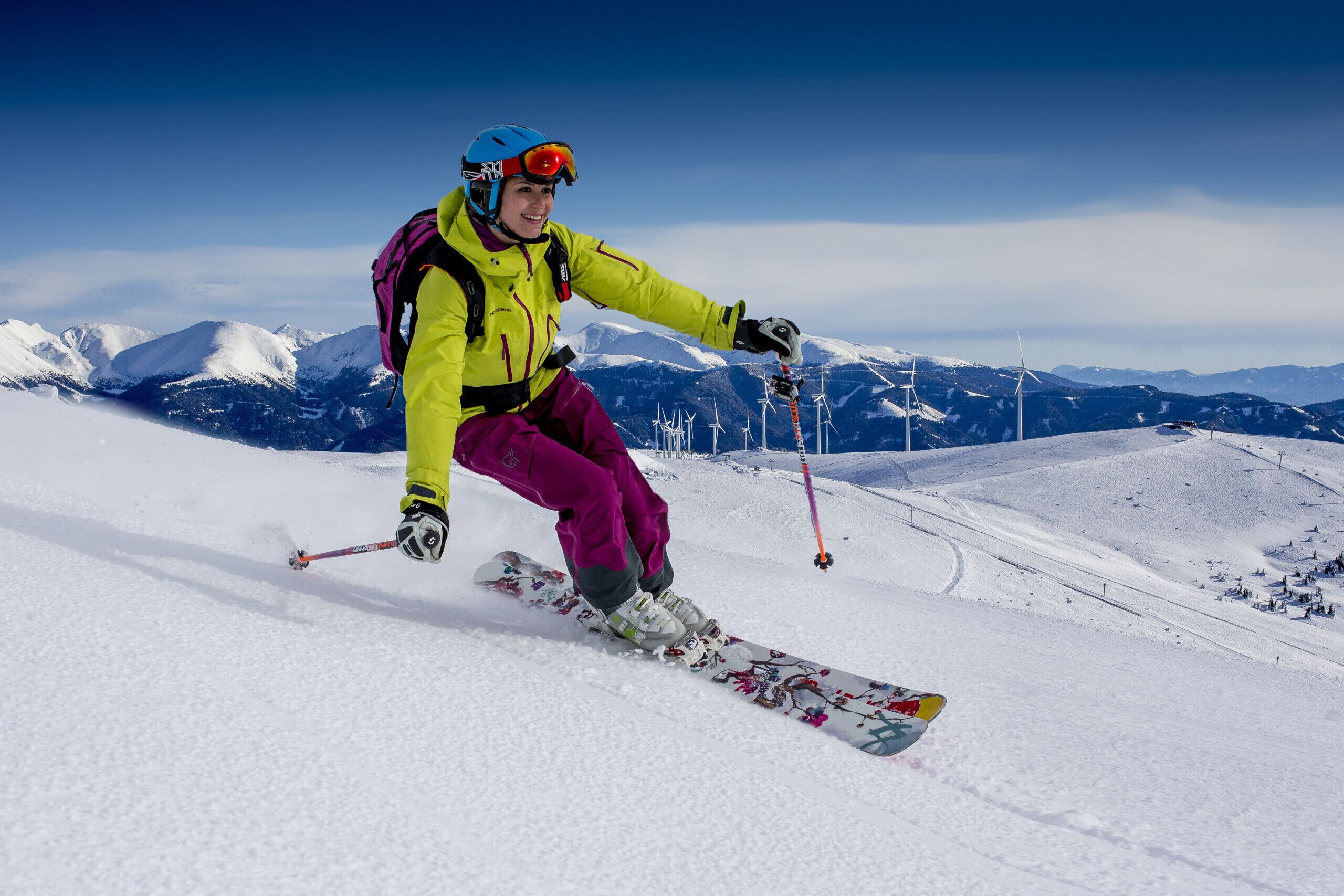 A person skiing on a snowy slope with a clear sky and mountains in the background.