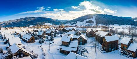 Un village enneigé avec des chalets en bois, une piste de ski et des montagnes en arrière-plan.