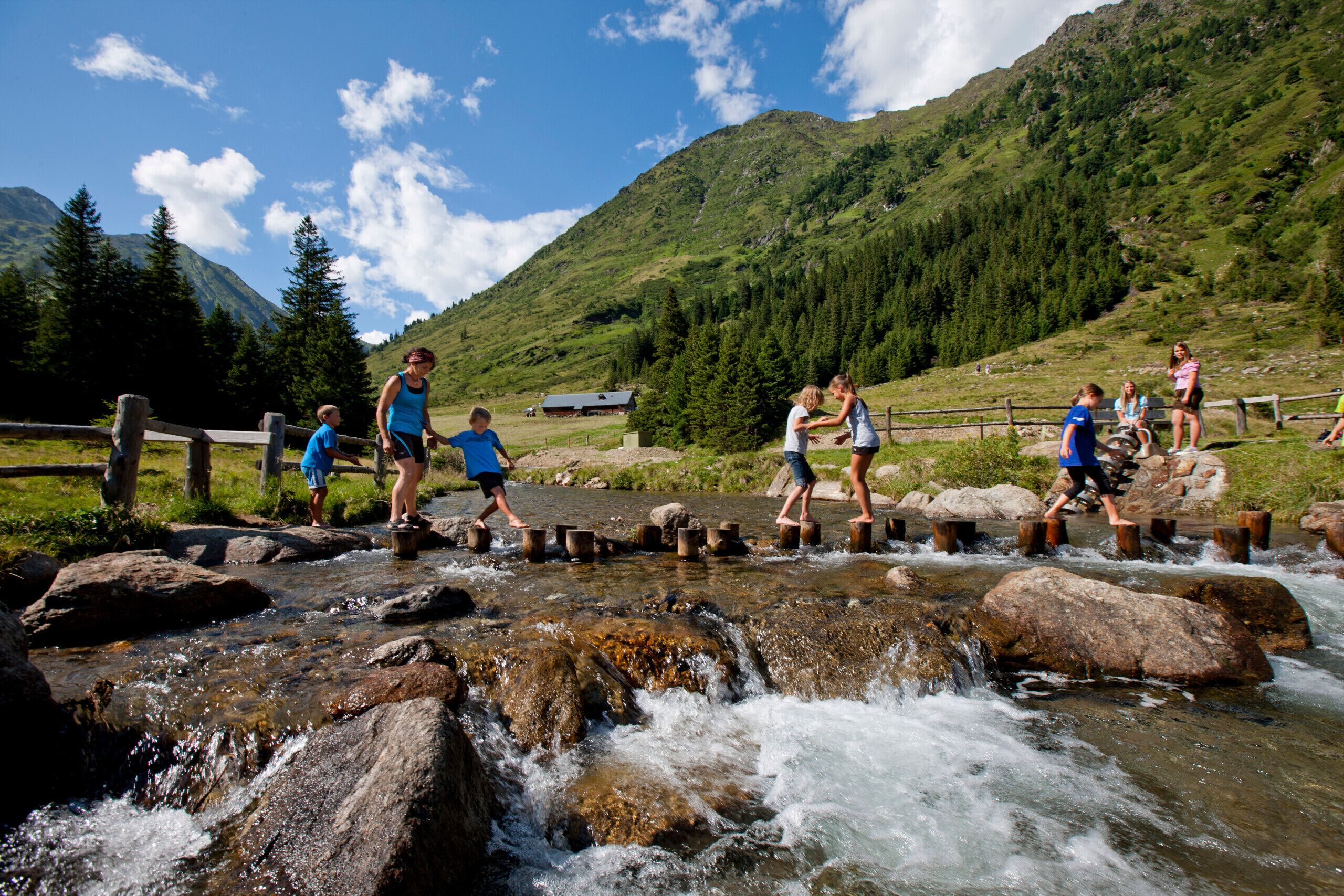A group of people crossing a stream over wooden planks.