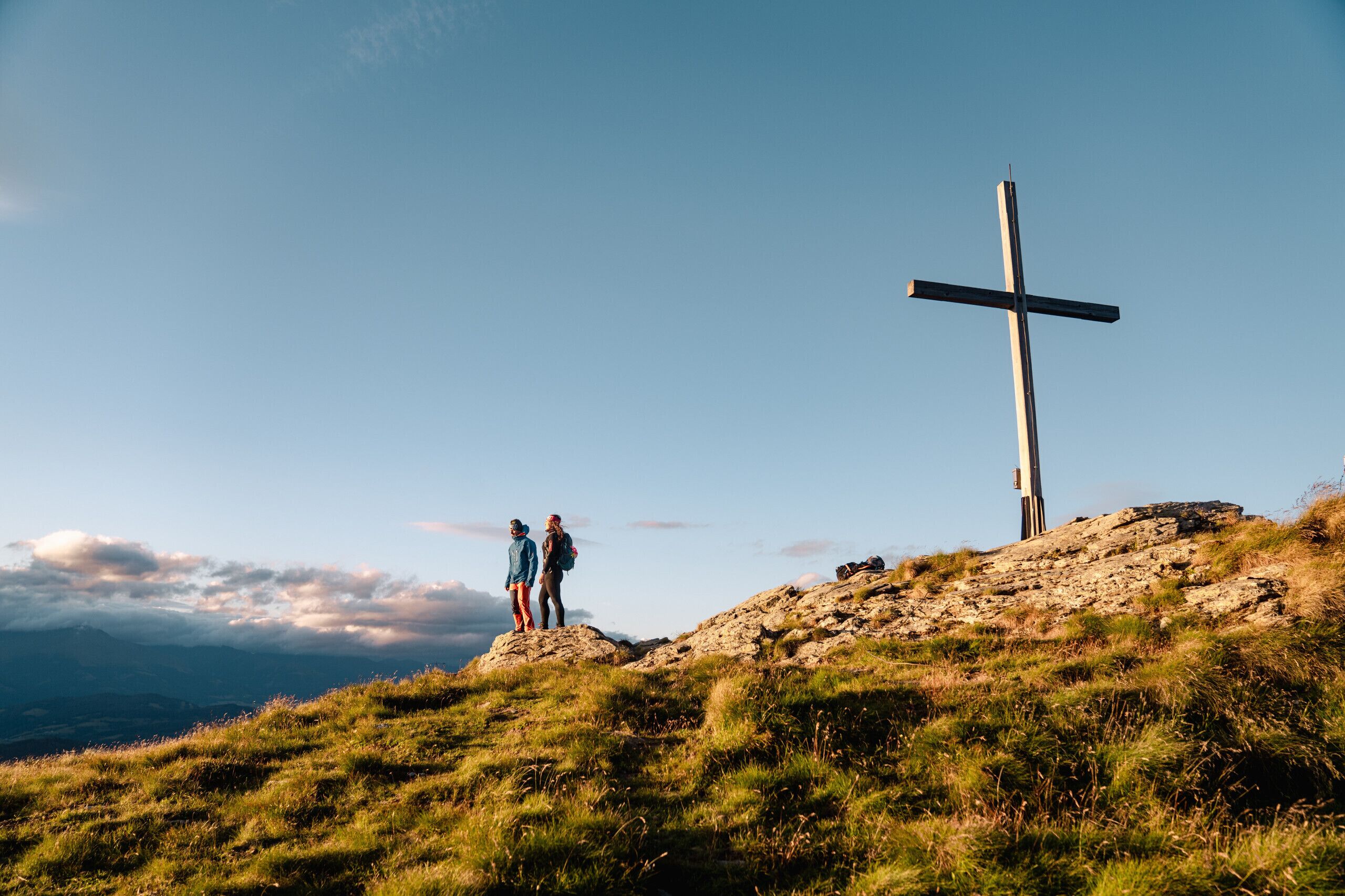A cross on a hill with two people standing nearby.
