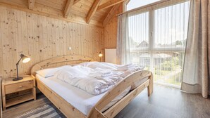 A wooden bedroom with a bed, nightstands, and a large window with curtains. - Apartment with 1 bedroom (St. Georgen am Kreischberg)