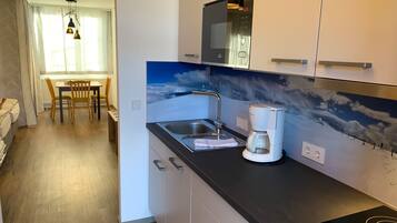 Et moderne køkken med indbygget mikrobølgeovn, kaffemaskine og vask. I baggrunden ses et spiseområde med bord og stole.