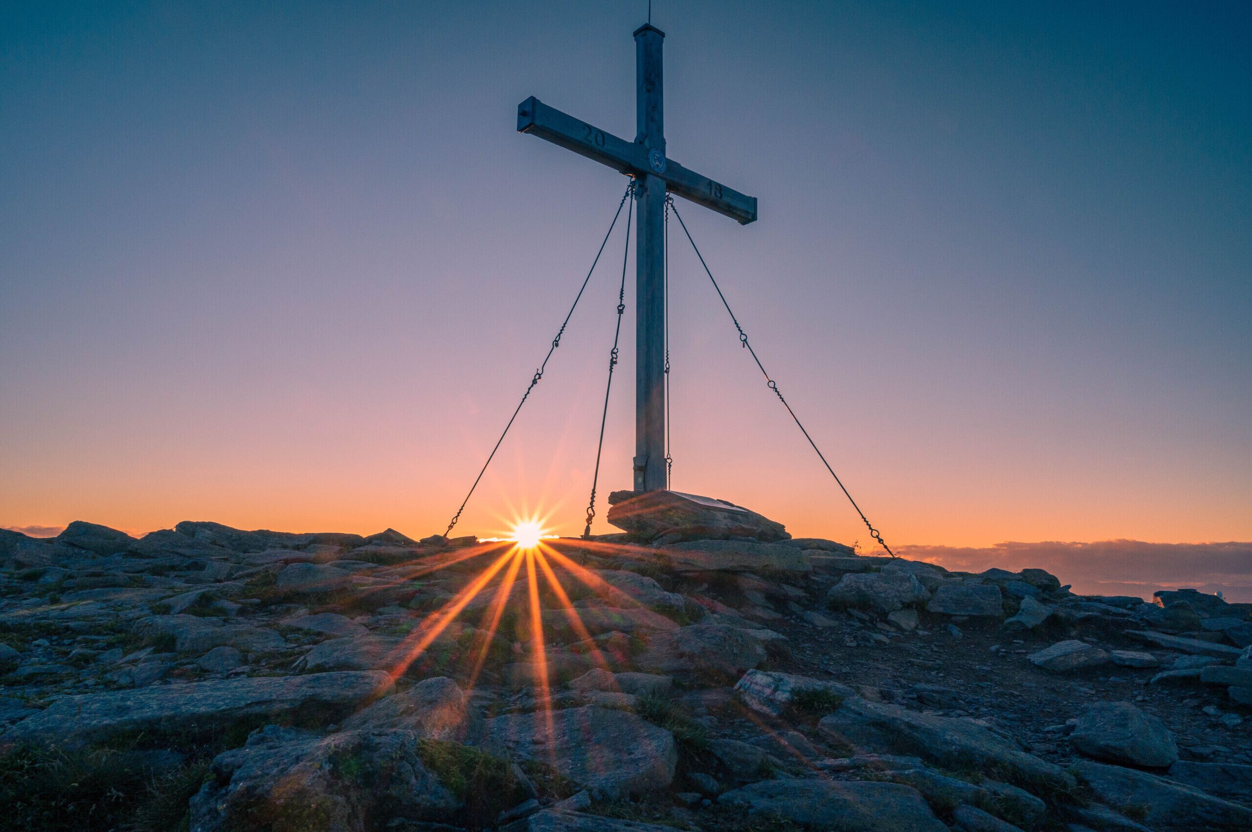 Risti kallioisella kielekkeellä, ja auringonlasku sen takana.