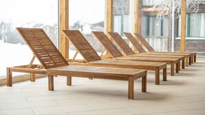 A row of wooden lounge chairs aligned in front of a large window with a view of snow-covered mountains.