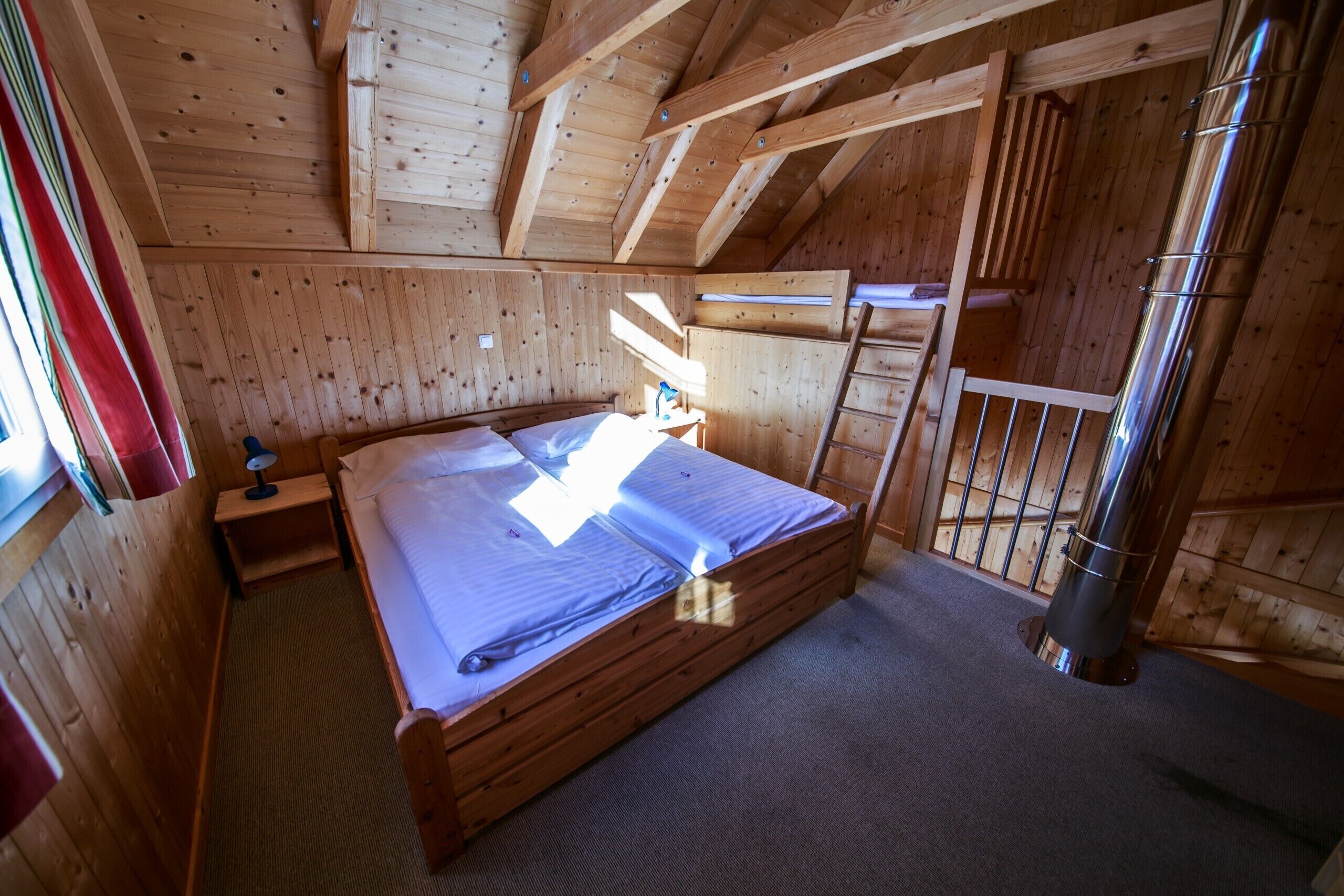 Una camera in una baita di legno, con un letto, un comodino e una finestra con tende.