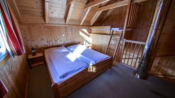 Una camera in una baita di legno, con un letto, un comodino e una finestra con tende.