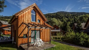 Eine Holzhütte mit einer Veranda, umgeben von üppigem Grün und einer Bergkulisse.