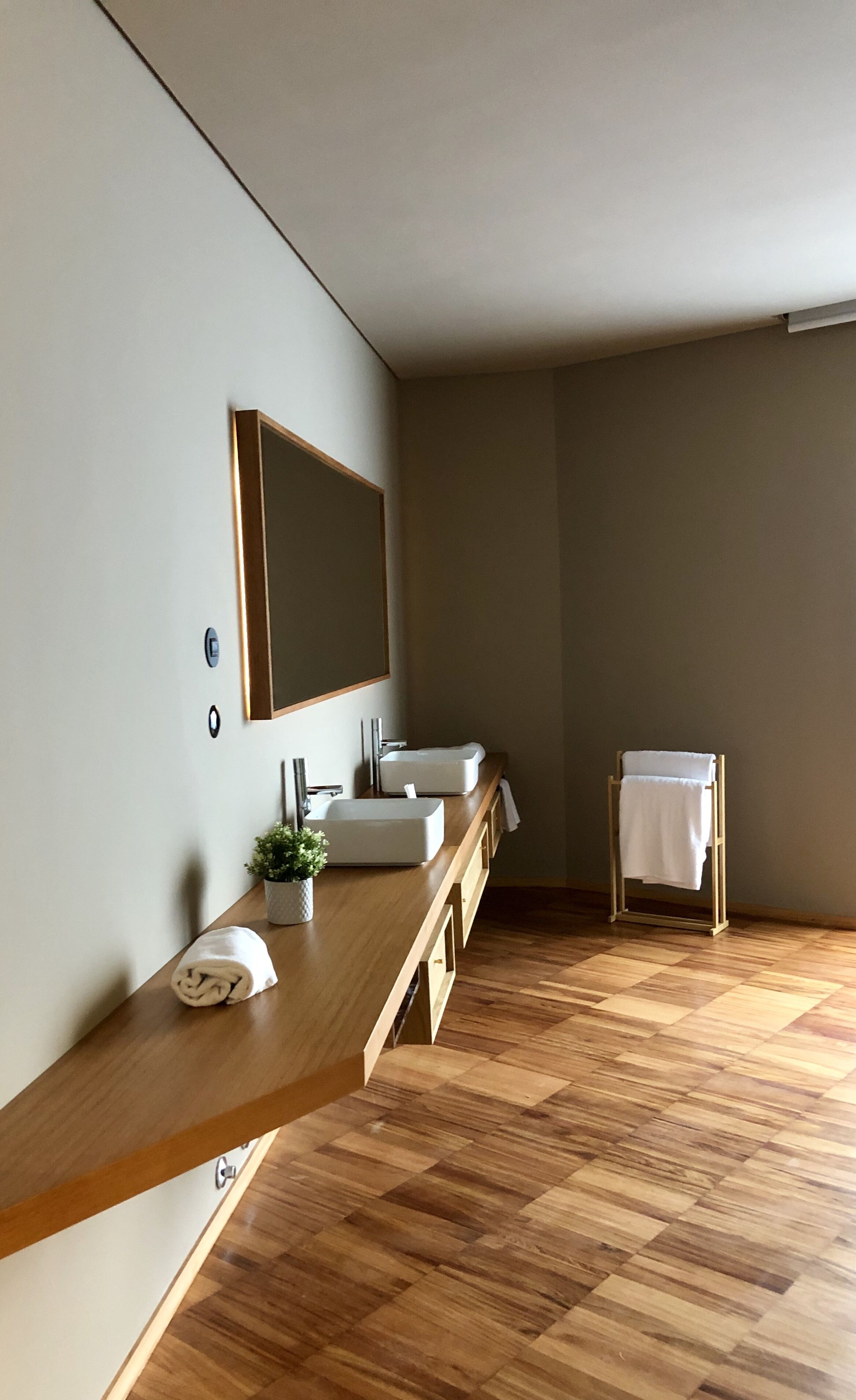 A modern bathroom with a wooden vanity, two sinks, a large mirror, and a towel rack.