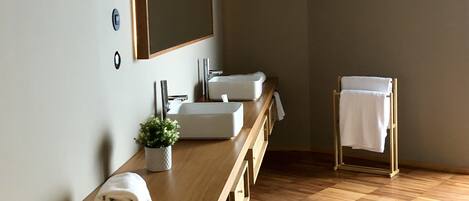 A modern bathroom with a wooden vanity, two sinks, a large mirror, and a towel rack.