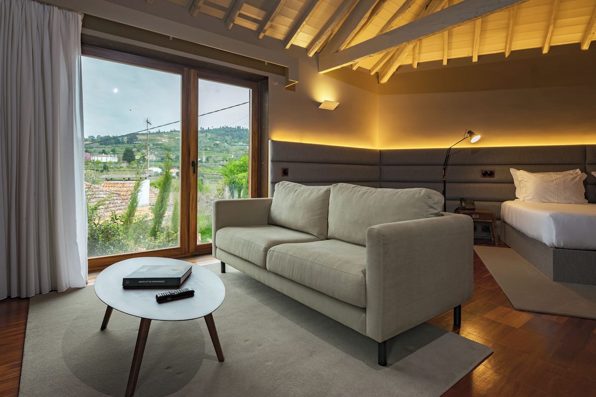 A modern bedroom with a sofa, a bedside table, a lamp, and a view of the outdoors.