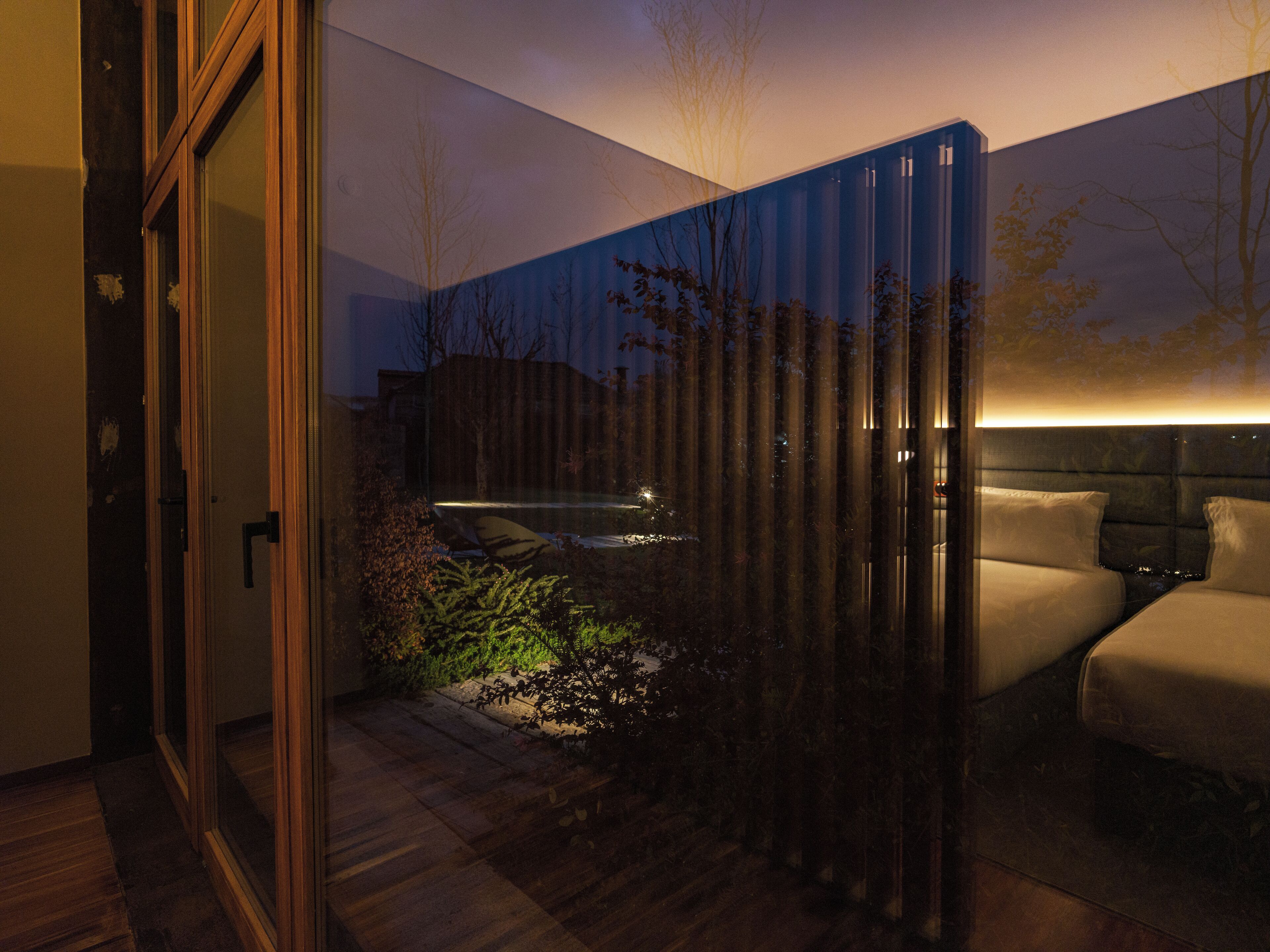 Une chambre moderne avec un grand lit, une table de chevet et une fenêtre donnant sur des arbres.