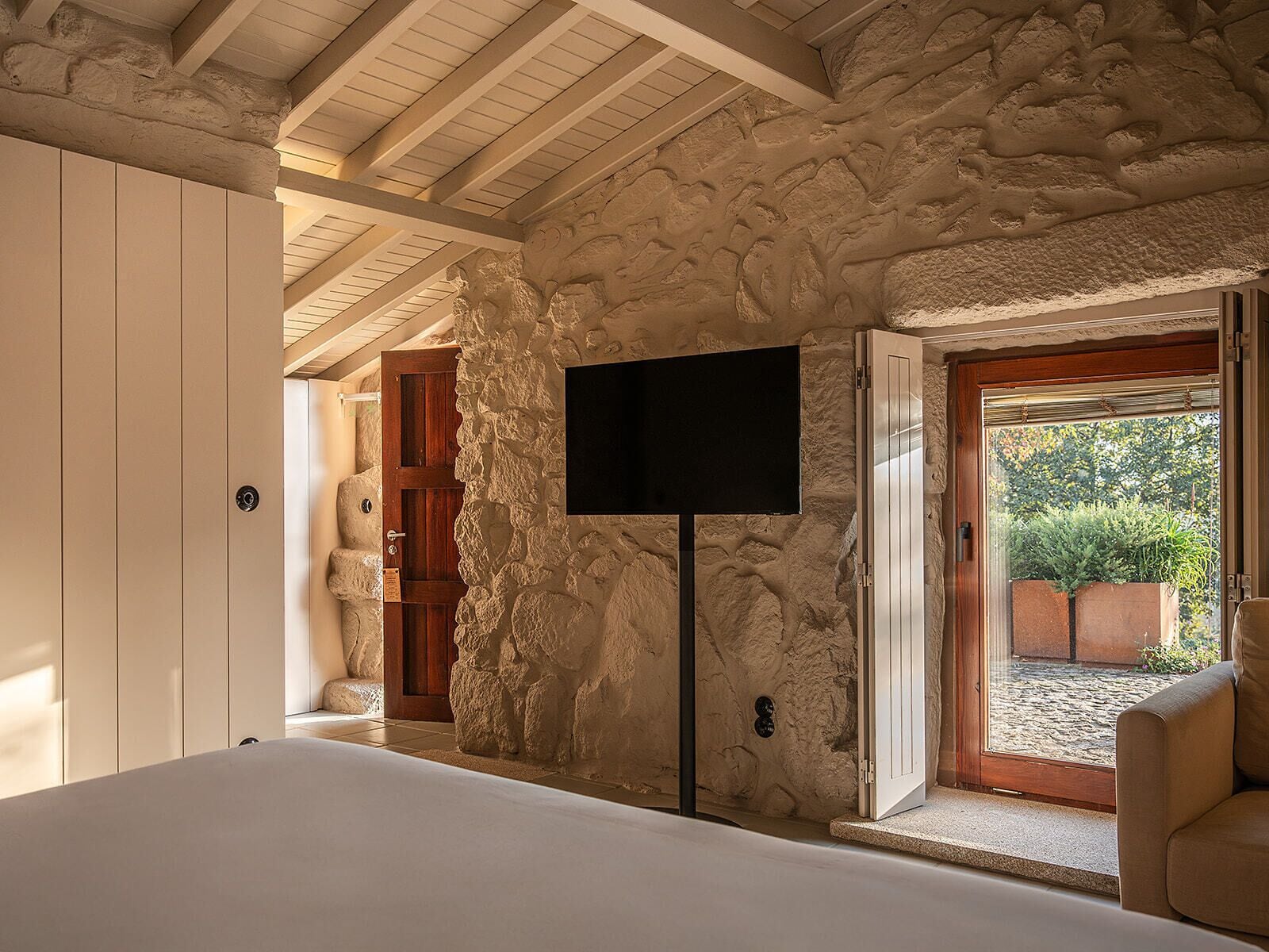 Ein Schlafzimmer mit Steinwand, Flachbildfernseher, Bett und Blick ins Freie.