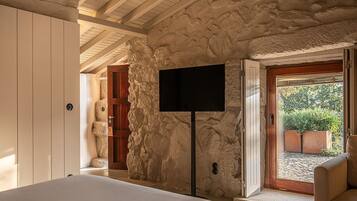 Ein Schlafzimmer mit Steinwand, Flachbildfernseher, Bett und Blick ins Freie.